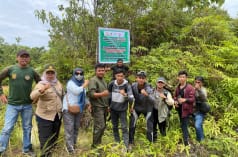 beberapa orang didepan tanda yang melarag semua kegiatan di hutan produksi