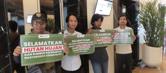 Empat warga dengan plakat bertuliskan “Selamatkan hutan hujan dan sumber kehidupan masyarakat Loeha Raya”