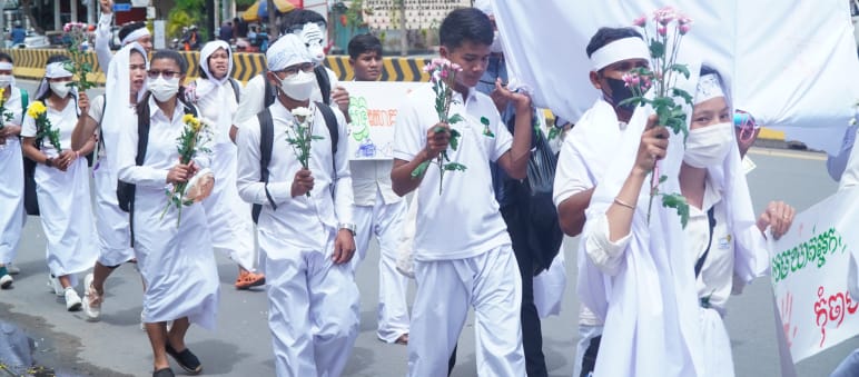 Sekelompok anak muda berpakaian putih berjalan dengan bunga di tangan melewati jalan di Phnom Penh