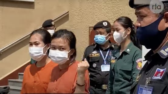 Dua tahanan perempuan dengan pakaian berkabung berwarna oranye, di belakangnya polisi