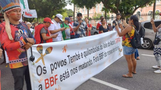 Aksi protes kelompok masyarakat adat dengan spanduk besar di sebuah jalan di sebuah kota: Tulisan di spanduk: Warga Temnbé dan Quilombola dari lembah Acará: BBF membunuh kami. BBF keluar dari wilayah kami