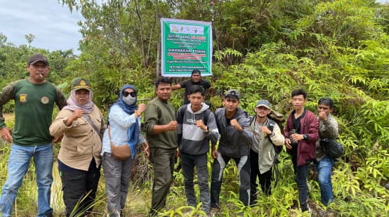 beberapa orang didepan tanda yang melarag semua kegiatan di hutan produksi