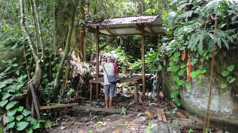 Sembahyang di depan altar di hutan, disampingnya terdapat tebing bebatuan dan dibawahnya aliran air kecil Altar di hutan hujan