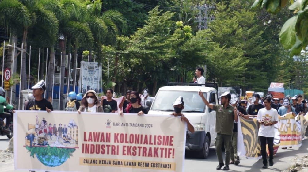 Demo – tampak depan: spanduk “Lawan Kolonialisme Industri Ekstraktif”, tampak belakang: peserta demo dan sebuah mobil pick-up